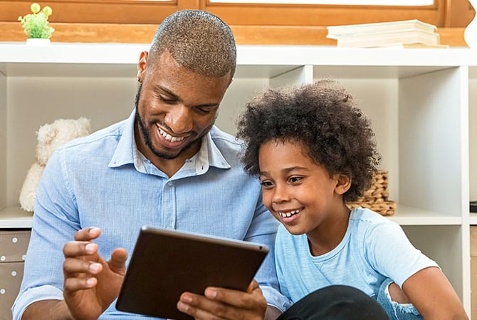 Mercado Pago: pai e filho olhando o tablet com um sorriso no rosto para escolher o presente de Dia das Crianças que será comprado.