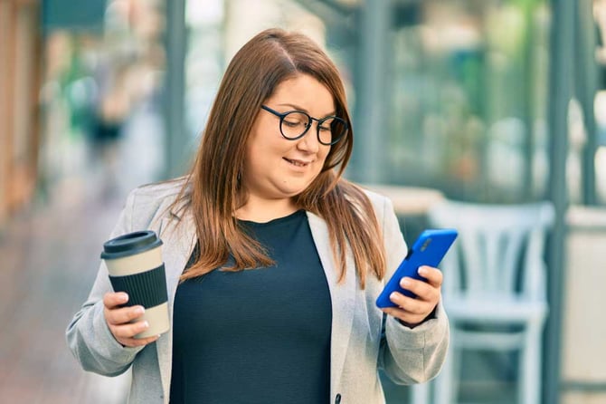 Mulher olhando para celular e segurando copo de café