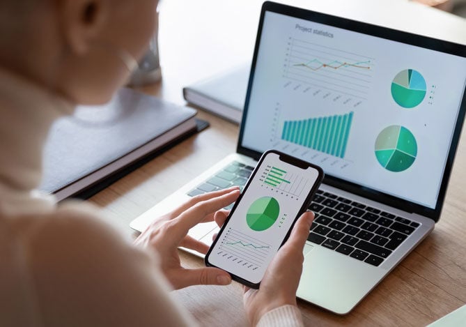 Mercado Pago: mãos de uma pessoa mexendo no celular enquanto analisa gráfico para alocação de recursos 