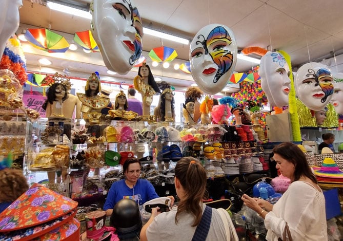 Mercado Pago: Loja decorada com itens carnavalescos, como máscaras e acessórios, repleta de clientes comprando durante o Carnaval, mostrando oportunidades de campanha de vendas.