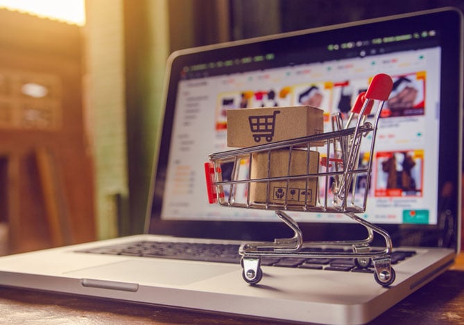 Mercado Pago: laptop aberto com uma tela mostrando uma espécie de catálogo online com um carrinho pequeno em cima dele com caixas dentro.