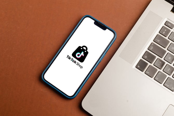 Mercado Pago: celular visto de cima com tela aberta no TikTok Shop, ao lado de um notebook, representando um empreendedor que está aprendendo como vender no TikTok. 