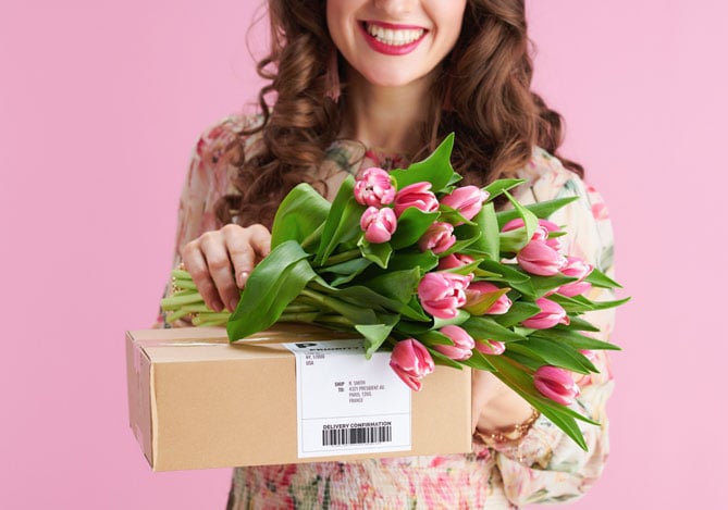Mercado Pago: imagem de uma mulher recebendo uma caixa e um buquê de tulipas rosas em comemoração ao Dia das Mães. A imagem ilustra o presente que teria sido comprado no negócio de um empreendedor que aproveitou a data para vender o kit de Dia das Mães como forma de fazer dinheiro extra.