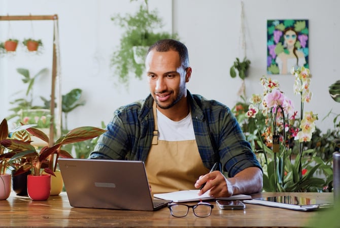 Mercado Pago: homem sentado à mesa em uma floricultura, com notebook em sua frente enquanto ele estuda a melhor solução de empréstimo para microempresa.