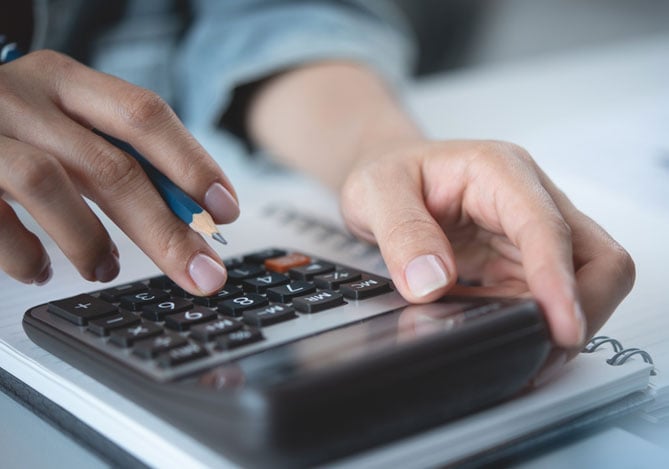 Mercado Pago: mãos digitando em uma calculadora apoiada em um caderno para fazer a gestão financeira do seu próprio negócio