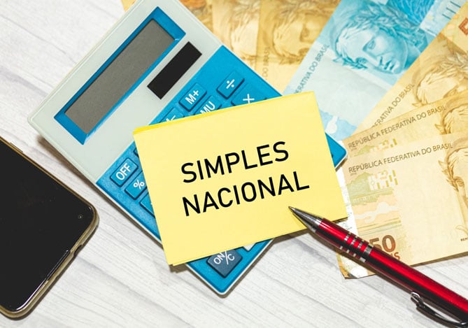 Mercado Pago: mesa com notas de dinheiro em real, calculadora, celular, caneta e um bilhete que sugere falar sobre a exclusão do Simples Nacional
