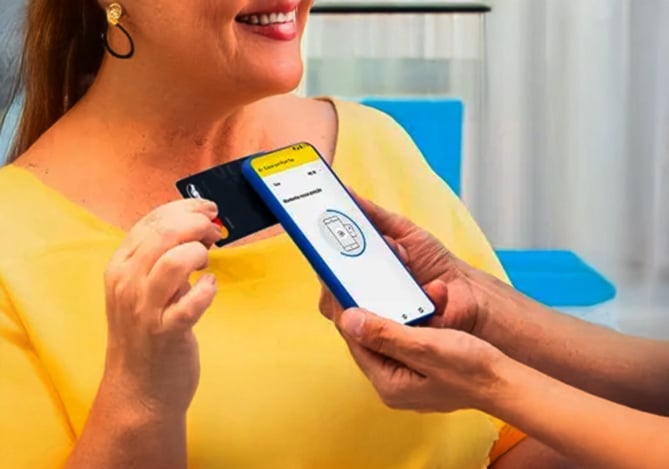 Mulher sorrindo, vestindo blusa amarela e encostando seu cartão de crédito Mercado Pago na maquininha no celular sem taxa, a Point Tap.