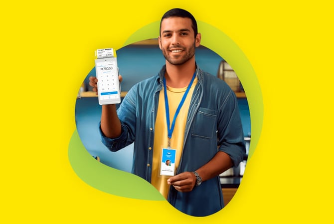 Mercado Pago: homem sorrindo, com crachá, uma camiseta amarela e uma camisa jeans por cima. Ele está segurando uma maquininha do Mercado Pago, representando o programa de revenda com um pitch de vendas elaborado. 