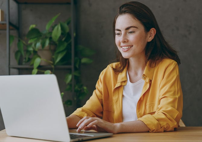 Mercado Pago: mulher sorridente usando notebook em ambiente moderno, representando a criação e atualização de seu portfólio digital para divulgar trabalhos ou serviços online.