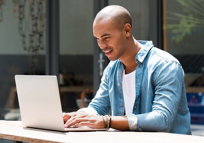 Mercado Pago: Jovem empreendedor trabalhando em um café ao ar livre com um laptop, demonstrando a importância da propriedade intelectual para proteger seu negócio digital e garantir exclusividade no mercado.
