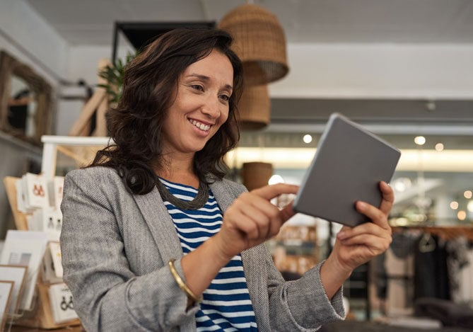 Empreendedora sorridente usando um tablet para gerenciar suas vendas no varejo, demonstrando como a tecnologia pode impulsionar a experiência do cliente.