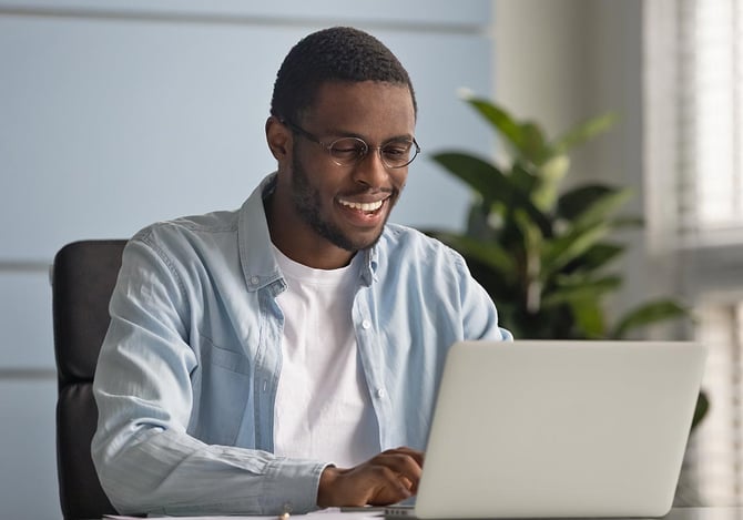 Homem de óculos sentado e sorrindo enquanto trabalha no laptop