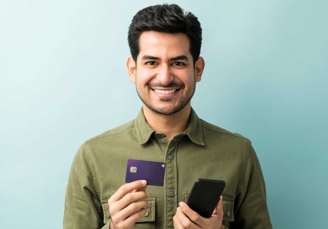Mercado Pago: Homem sorridente segurando cartão de crédito para MEI em uma mão e na outra o celular