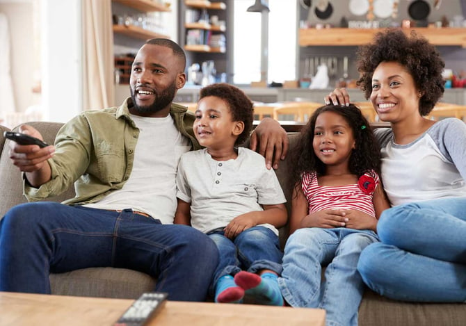 Família sentada no sofá assistindo TV