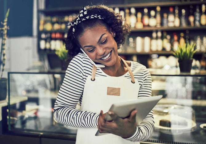 Mulher sorrindo enquanto fala no celular e mexe no tablet