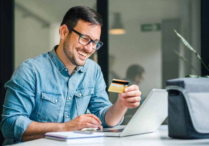 Mercado Pago: empreendedor sentando em mesa de escritório com notebook aberto e cartão na mão solicitando crédito empresarial