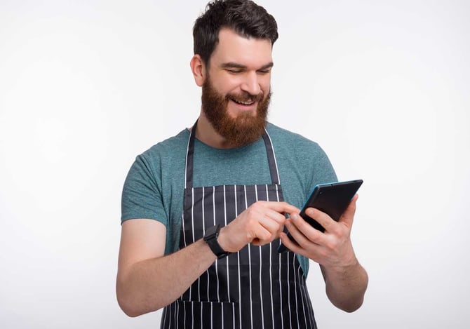 Homem sorridente com um avental mexendo em um tablet