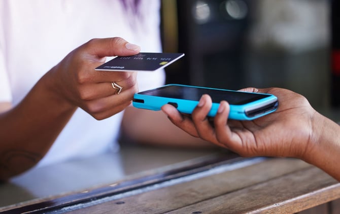 Mercado Pago: mão de empreendedor cobrando de seu cliente utilizando a Point Tap em seu celular para aumentar as vendas