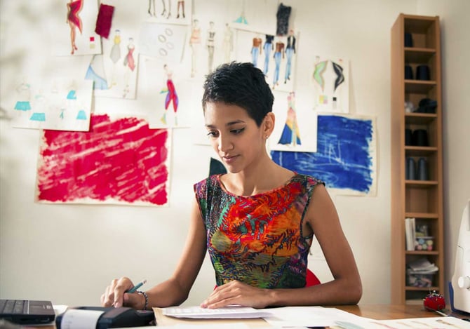 Mulher sentada com a mesa com relatórios e fazendo contas na calculadora