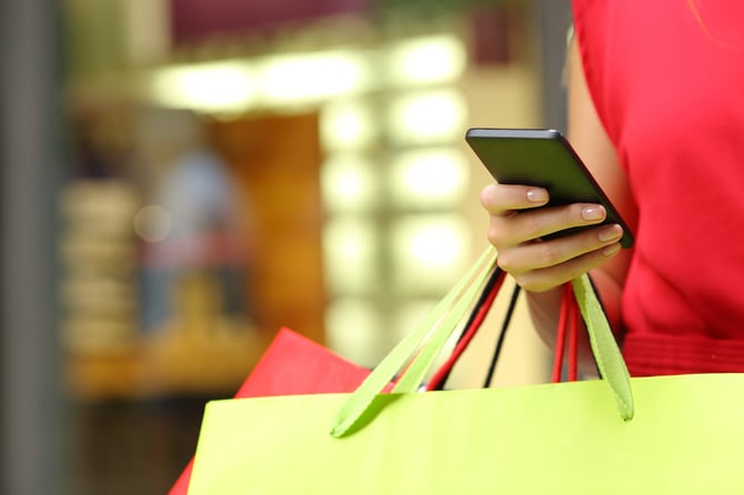 Mercado Pago: mãos de mulher com sacolas de compras e celular em mãos procurando como vender sem site