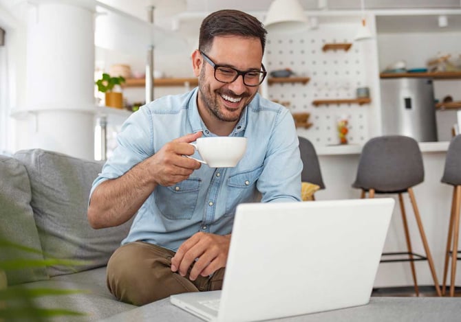 Homem sorridente olhando para o notebook segurando uma xícara