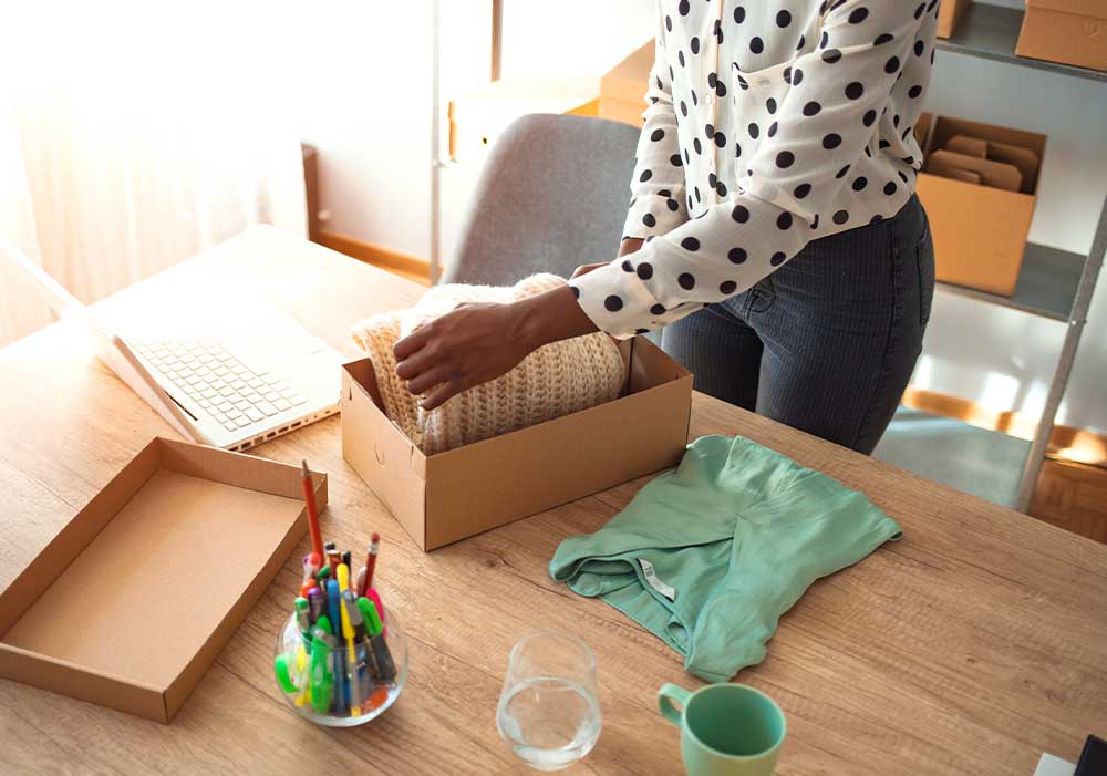 Mulher de coque dobrando uma camisa azul ao lado de uma caixa com outras peças de roupa