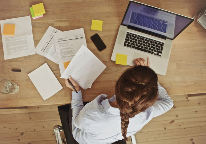 Mercado Pago: imagem vista de cima de uma mulher empreendedora, em uma mesa de trabalho, com um notebook, separando os documentos para declarar imposto de renda.