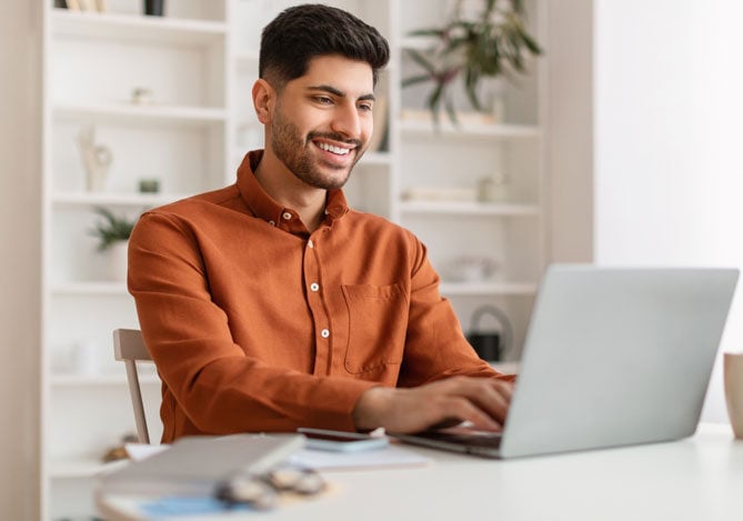 Mercado Pago: imagem de um empreendedor vestindo camisa de manga longa sentado à mesa enquanto usa seu notebook para acessar o Domicílio Eletrônico Trabalhista (DET) para verificar se há mensagens novas relacionadas ao seu MEI.