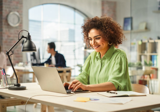 Mulher vestindo uma camisa amarela sentada em um escritório enquanto faz uma busca em seu laptop relacionada ao Dropshipping Mercado Pago