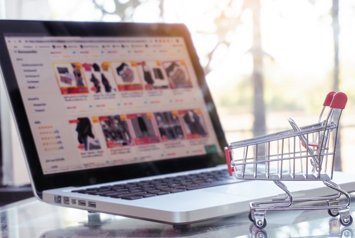 Mercado Pago: notebook aberto em em sites de marketplaces, com um mini carrinho na frente, representando um dropshipping.