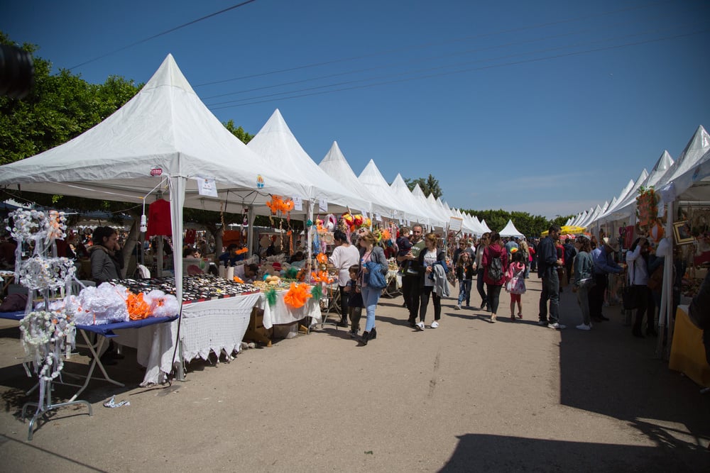 Feira de rua com várias barraquinhas com o que vender na rua e pessoas caminhando sugerindo celebração de Carnaval com o Mercado Pago