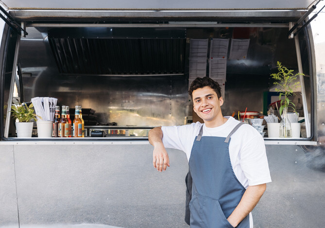 Mercado Pago: empreendedor vestindo camiseta branca e avental azul, que pesquisou anteriormente quanto custa para abrir um MEI e abriu um negócio de food truck.