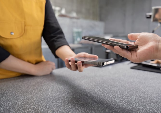 Mercado Pago: mão de cliente aproximando o celular ao smartphone do vendedor, que vai receber pelo celular como se fosse uma maquininha de cartão.