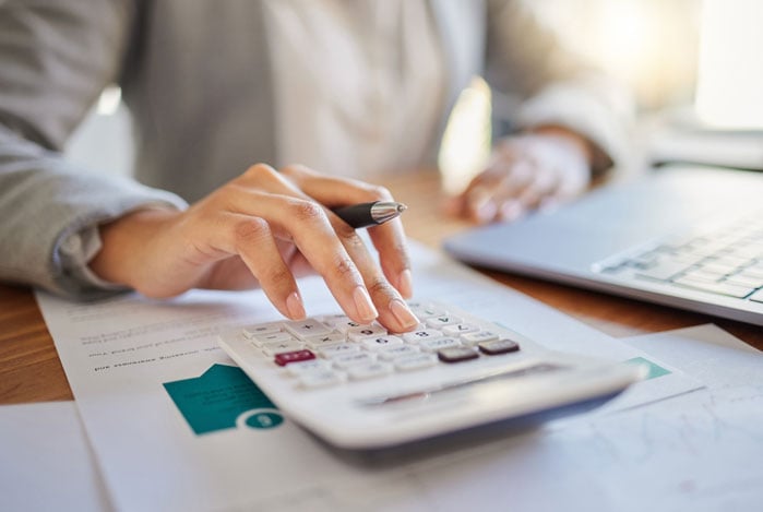 Mercado Pago: mãos digitando em calculadora, com papéis e notebook juntos na bancada para resolver a crise financeira de um negócio