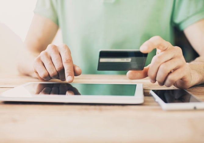 Mercado Pago: mãos de uma pessoa mexendo no tablet para garantir o sistema antifraude da sua loja online e a outra mão segura o cartão de crédito.
