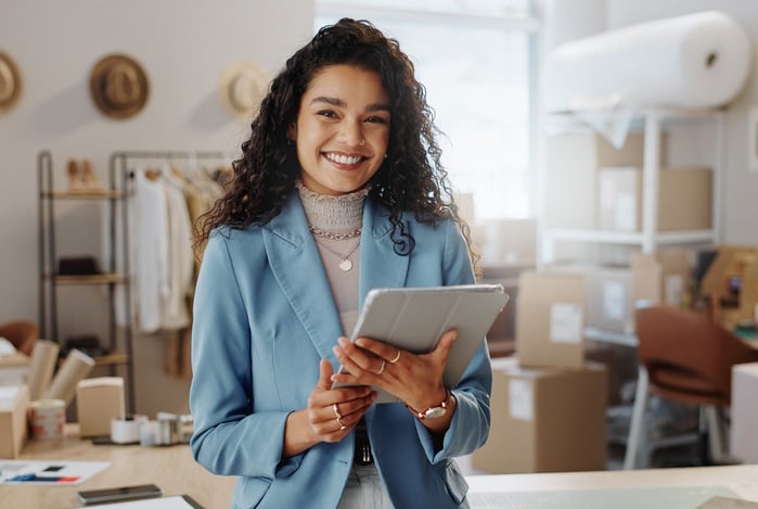 Mercado Pago: mulher em atelier, sorrindo para a câmera enquanto segura seu tablet para implementar um sistema de vendas recorrente em seu negóico.