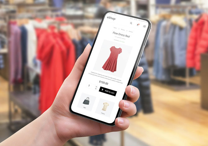 Mercado Pago: imagem da mão de uma pessoa segurando um celular para a realização de uma compra. Na imagem é possível ver a página de checkout para a finalização da compra após as festas de fim de ano de um vestido vermelho. Ao fundo da imagem, é possível ver o ambiente de uma loja de roupas, com araras e roupas penduradas.