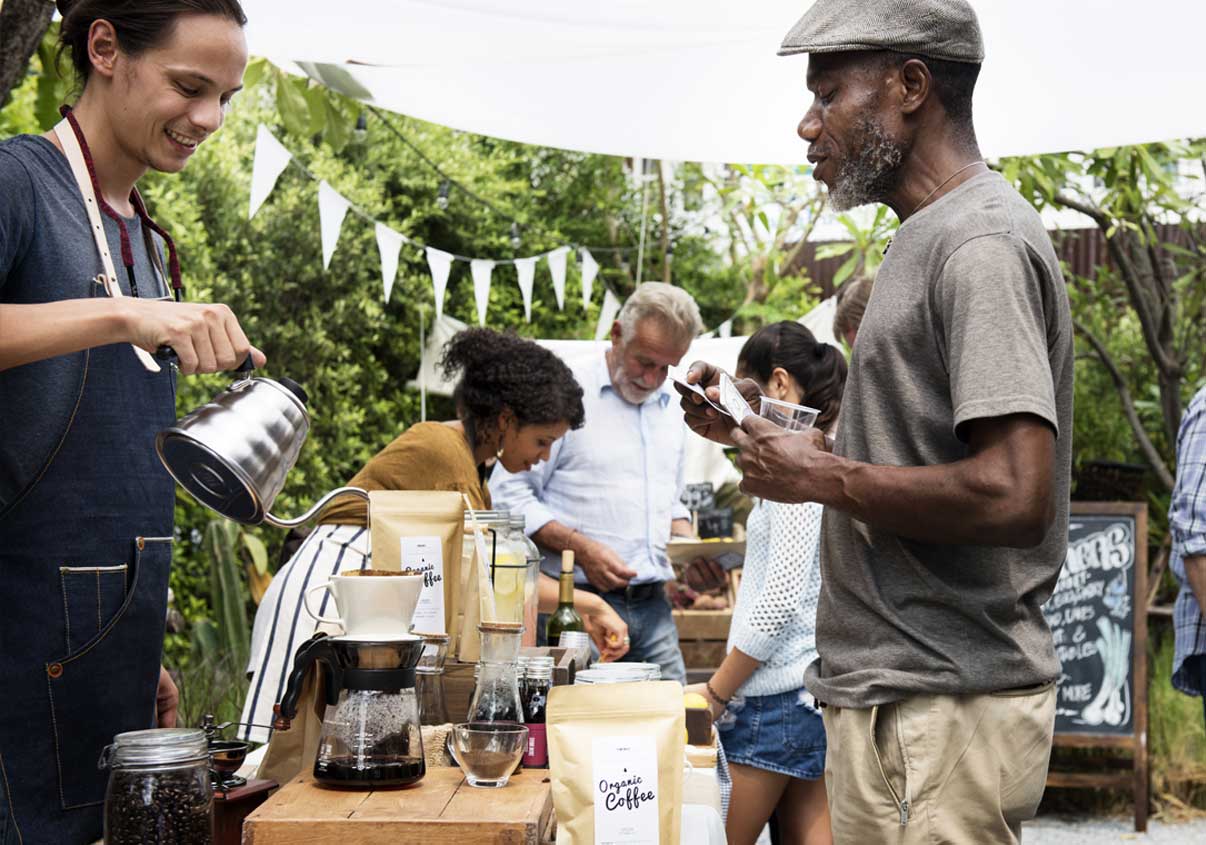 Homem sorrindo e servindo café para seu cliente em uma feira ao ar livre