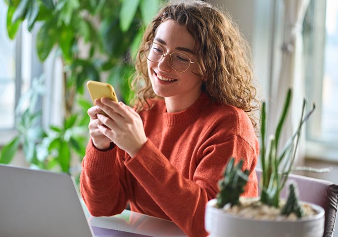 Mercado Pago: empreendedora sentada em sua mesa de trabalho com celular na mão pesquisando sobre venture capital para seu dropshipping